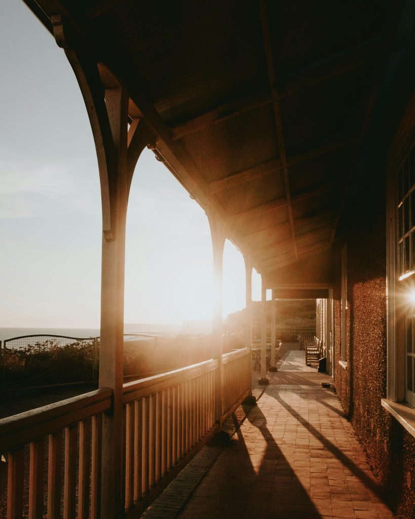 A cozy wooden balcony lit by warm morning sunlight, offering a scenic outdoor view.