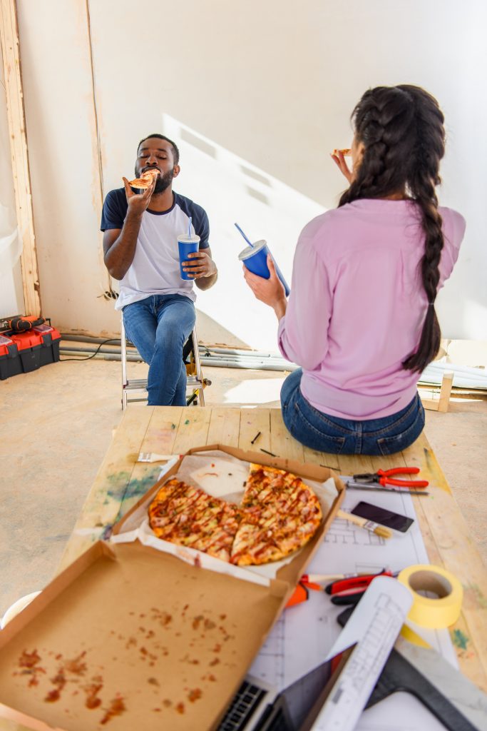 african american couple having lunch with pizza and soda during renovation at home A young couple enjoys pizza while taking a break from working on their home improvement decisions.