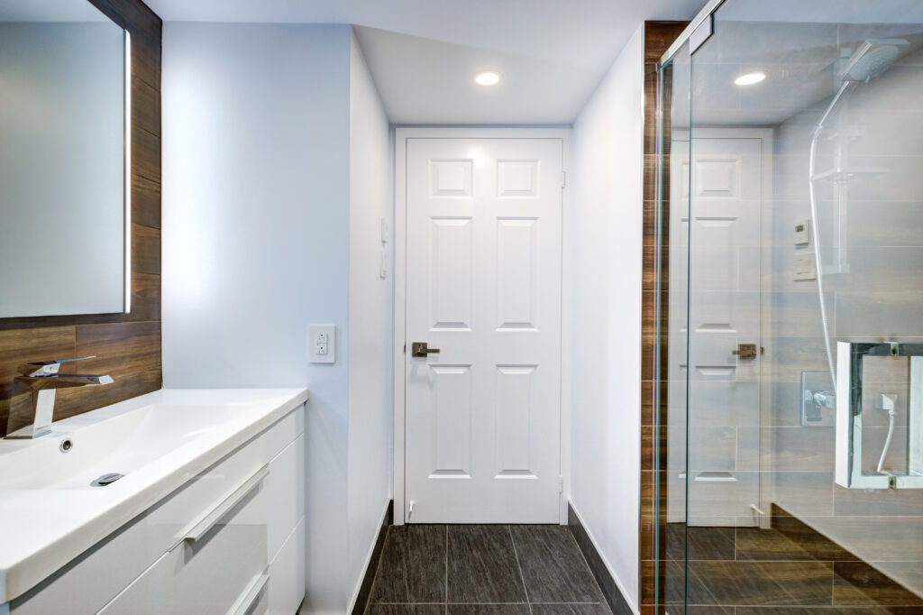 bathroom remodeling in Salem VA: This is a pristine, modern bathroom featuring a white sink and vanity, complemented by dark gray tile flooring and wood paneling.
